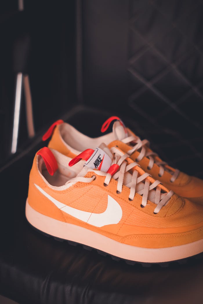 category-02 Stylish orange sneakers with white swoosh against a dark leather backdrop.